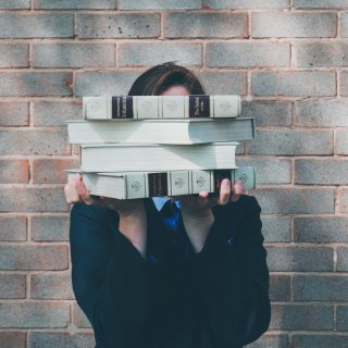 Siora Photography | Unsplash Woman holds stack of books in front of face.