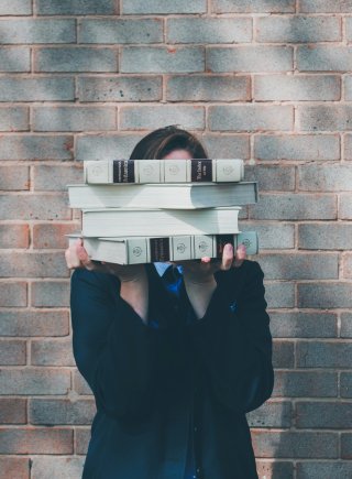 Siora Photography | Unsplash Woman holds stack of books in front of face.